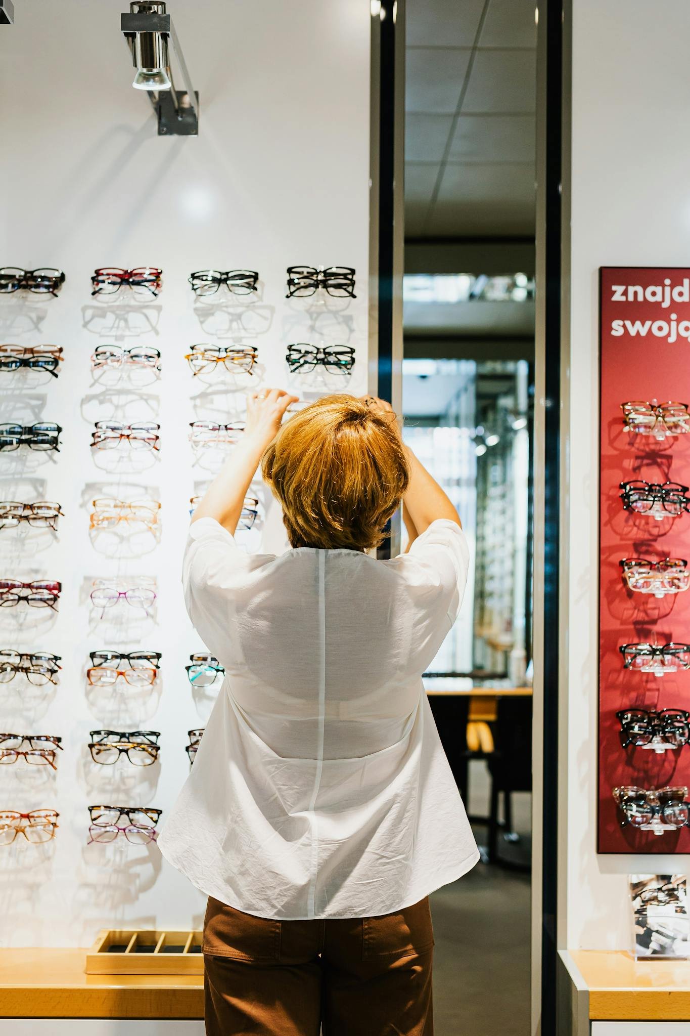 Back view of a woman browsing eyeglasses on a display in an optical store.