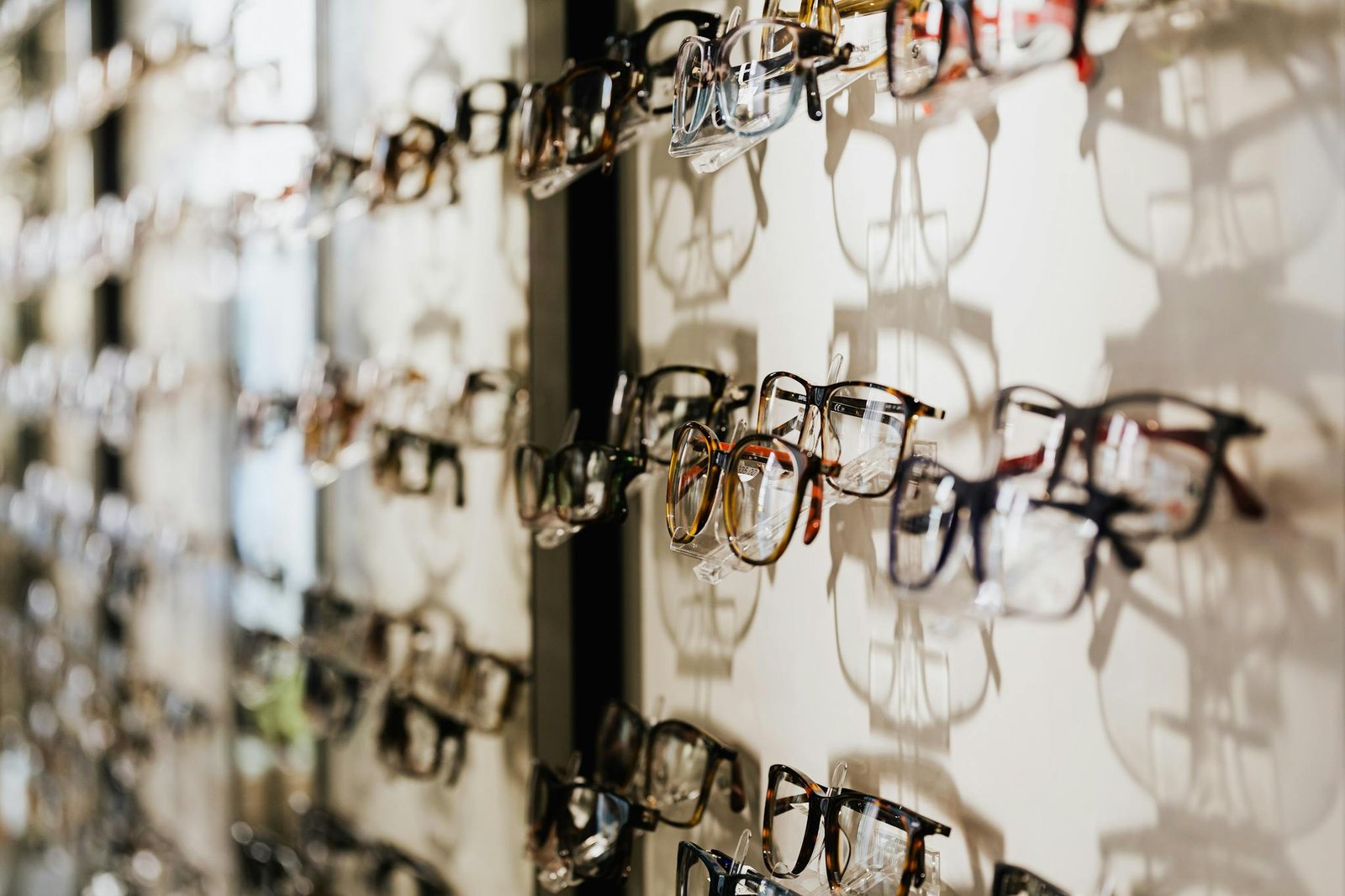 Wall-mounted display of diverse eyeglasses in a store setting with elegant shadows.